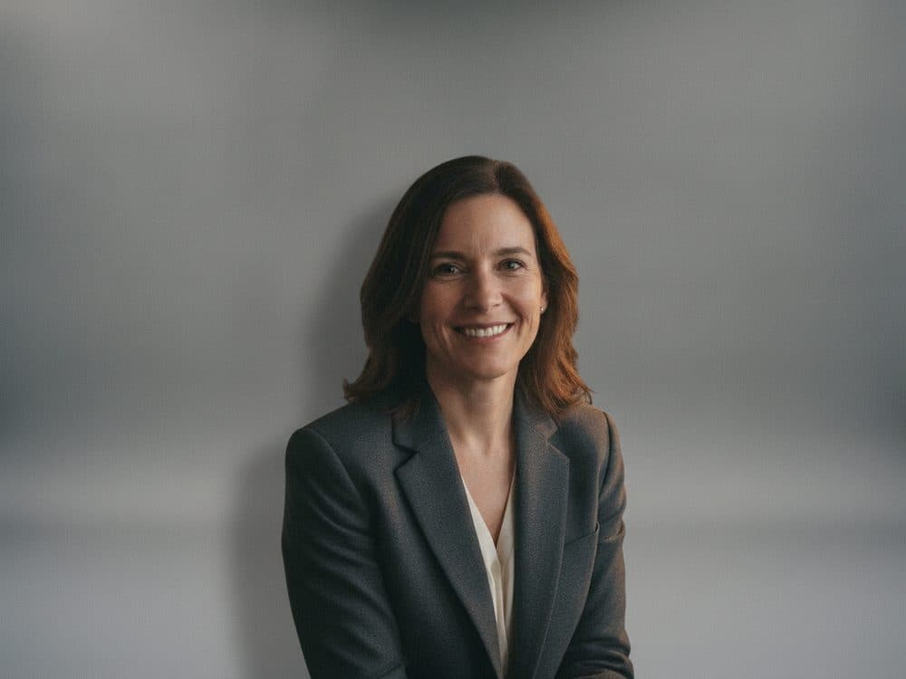 A woman in a blazer photographed against a clean grey studio backdrop instead of a cluttered room