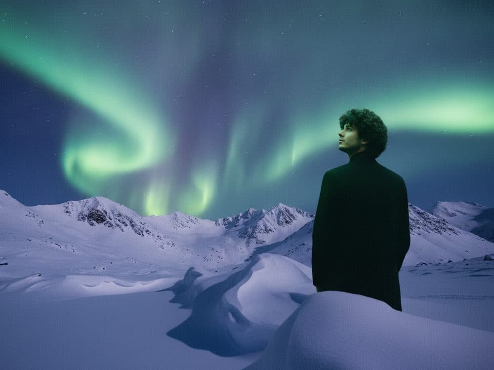 A man standing in snow beneath the northern lights